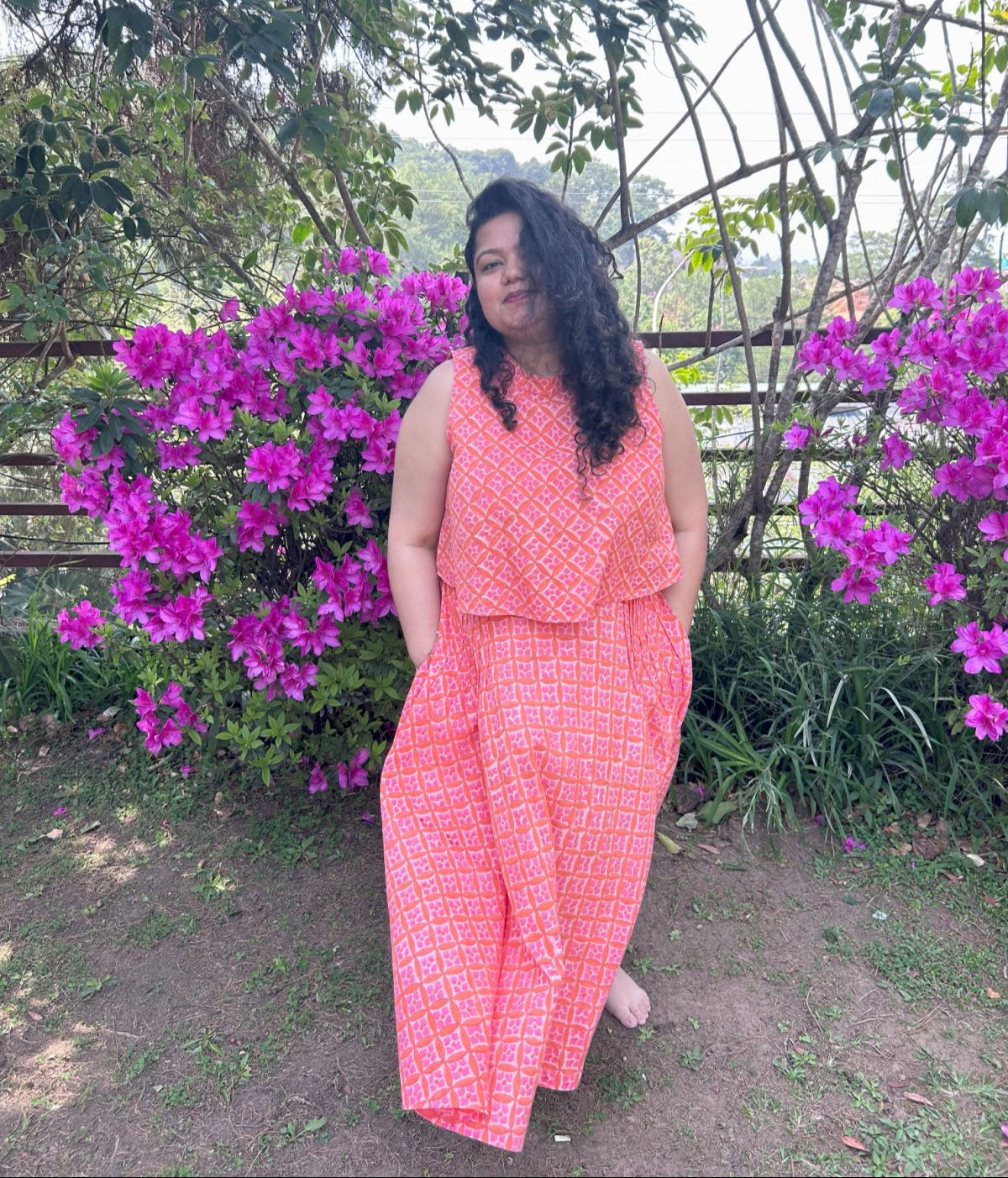 Woman in a coral outfit standing in front of pink flowers and greenery
